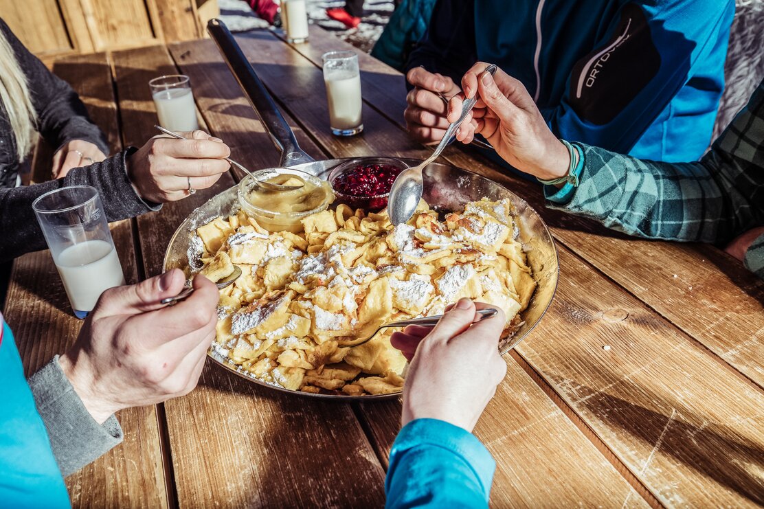 Auf diesem Bild zu sehen ist eine Pfanne voller Kaiserschmarrn mit einer kleinen Schüssel Apfelmus und einer kleinen Schüssel Preiselbeeren | © Ski Juwel Alpbachtal Wildschönau | shootandstyle 
