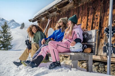 Zwei Frauen und ein Mann sitzen auf einer Bank neben einer Hütte - ihre Ski lehnen an der Hütte. | © Ski Juwel Alpbachtal Wildschönau | Christoph Oberschneider