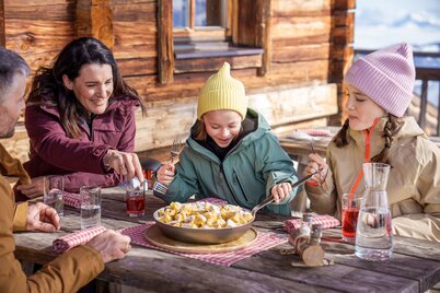 Zwei Erwachsene und zwei Mädchen auf einer Hütte beim Kaiserschmarrn essen. | © Ski Juwel Alpbachtal Wildschönau | Christoph Oberschneider