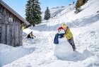 Ein Kind umarmt einen Schneemann während der Vater im Hintergrund im Schnee kniet. | © Ski Juwel Alpbachtal Wildschönau | Christoph Oberschneider