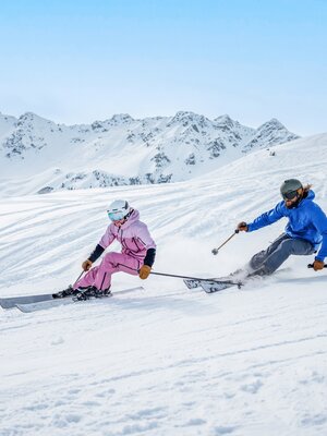 Ein Mann und eine Frau auf der Piste beim Skifahren mit Panorama im Hintergrund. | © Ski Juwel Alpbachtal Wildschönau | Christoph Oberschneider
