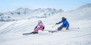 Ein Mann und eine Frau auf der Piste beim Skifahren mit Panorama im Hintergrund. | © Ski Juwel Alpbachtal Wildschönau | Christoph Oberschneider
