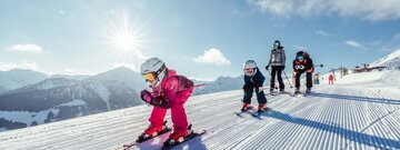 eine Familie fährt gemeinsam der Skipiste in Alpbach entlang, die Kinder fahren vor, die Eltern hinten nach  | © Alpbachtal Tourismus | shootandstyle 