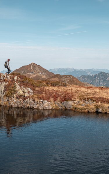 Auf diesem Bild zu sehen sind drei Personen, welche gerade an einem Bergsee entlang wandern, im Hintergrund die Berge  | © Alpbachtal Tourismus | shootandstyle 